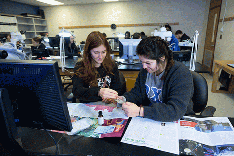 Two femal students working on at a desk in a lab analyzing fingerprints in the criminology class